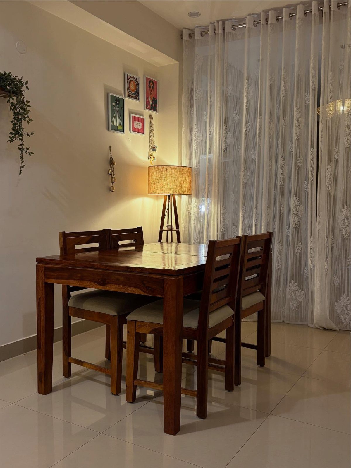 Wooden dining table and four chairs in a brightly lit room with white curtains.