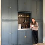 Woman standing by a dark grey-blue IKEA Havsta coffee nook with gold hardware.