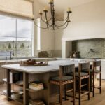 Large white marble kitchen island with wooden shelving and three matching bar stools.