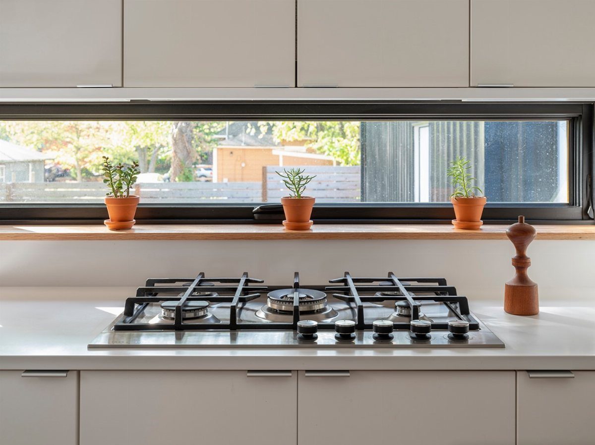 Long narrow kitchen window with black frame and small potted plants on wooden ledge