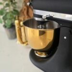 Matte black KitchenAid stand mixer with a shiny gold mixing bowl on white counter.