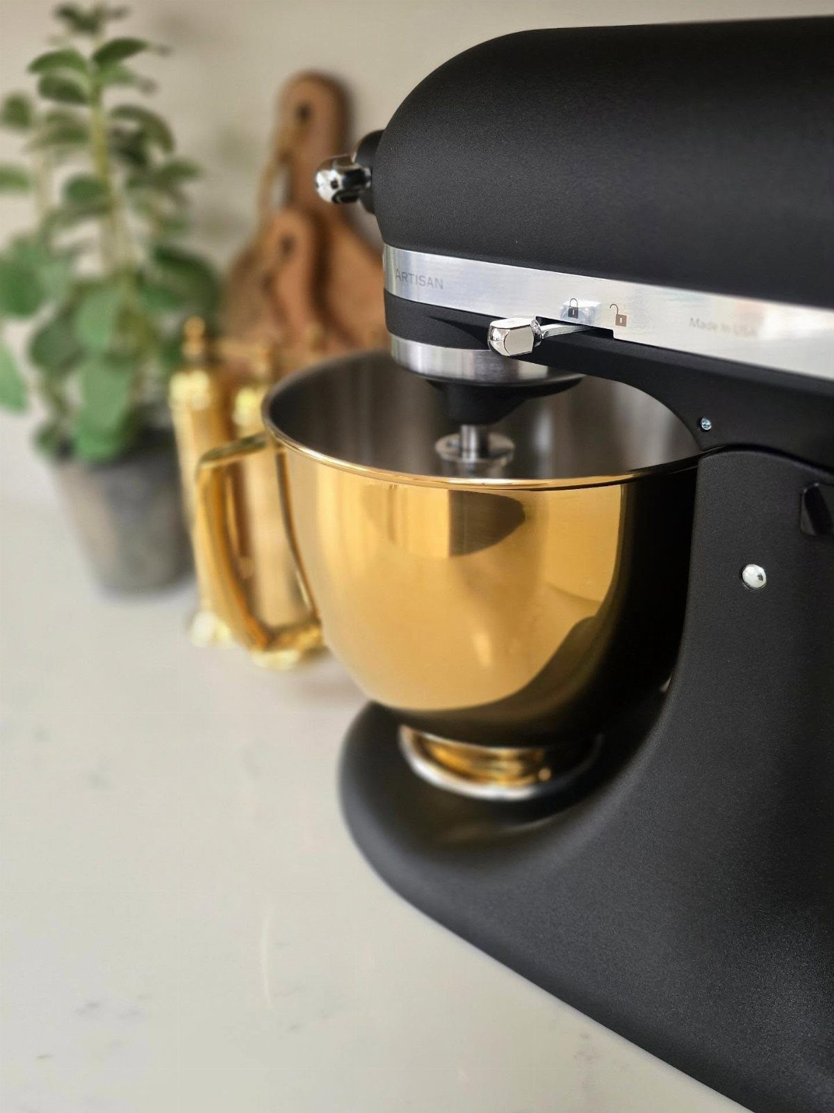 Matte black KitchenAid stand mixer with a shiny gold mixing bowl on white counter.