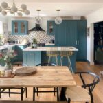 Wooden dining table and bench in a modern kitchen with teal cabinetry.
