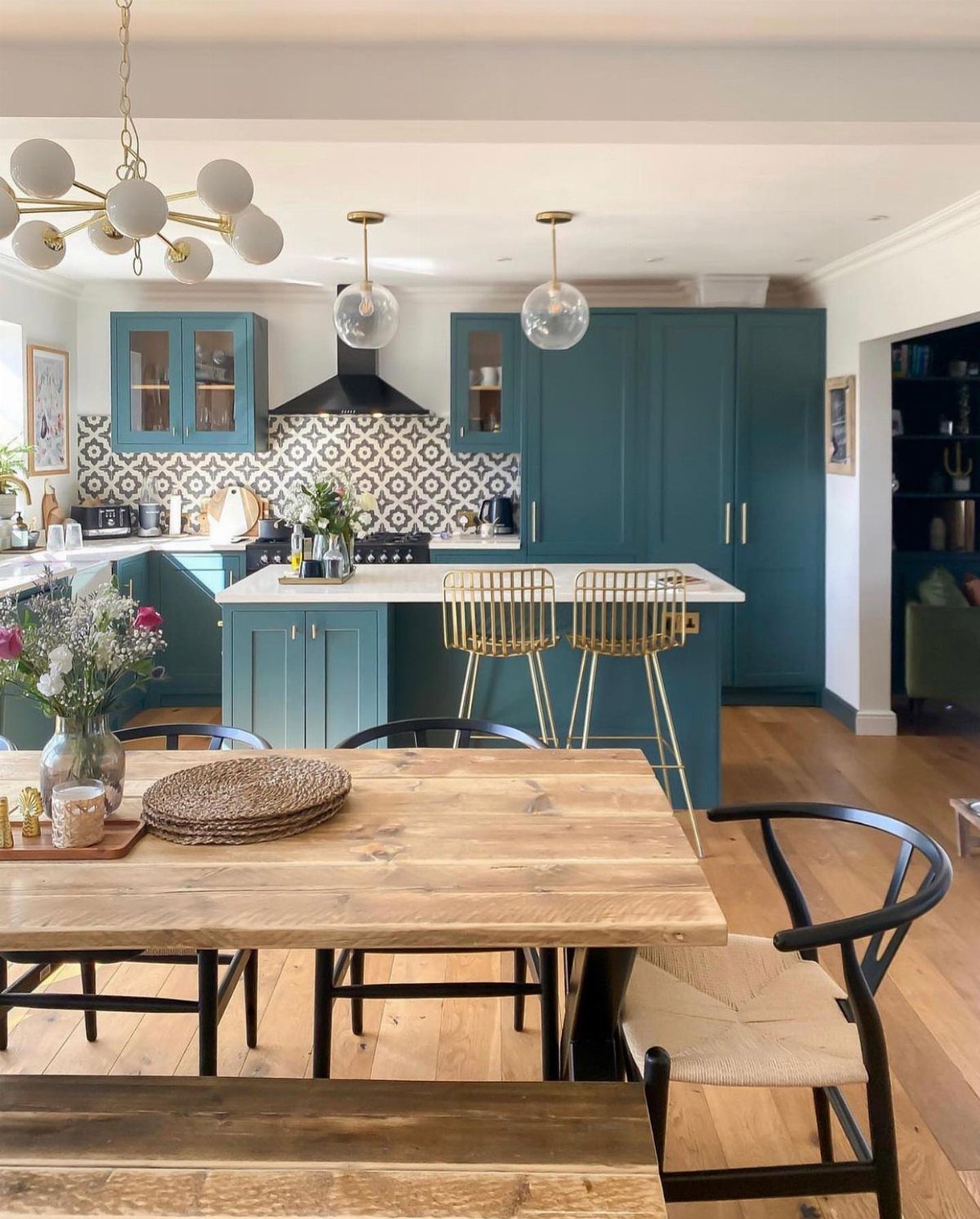 Wooden dining table and bench in a modern kitchen with teal cabinetry.