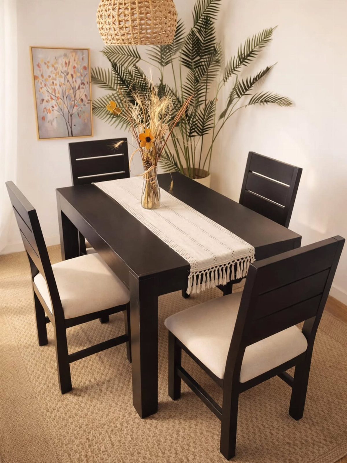 Black wooden dining table set with four cream cushioned chairs and a white runner.